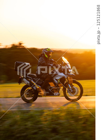 Driver riding motorcycle on empty road during sunset, spring mountains 125121868