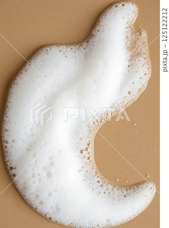Fluffy white foam in droplet shape on light brown background with soft texture 125122212