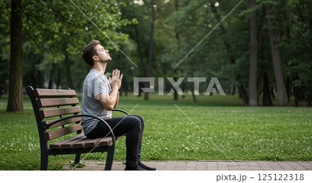Young man practicing deep breathing on park bench surrounded by lush greenery in morning Young man practicing deep breathing on park bench surrounded by lush greenery in morning 125122318