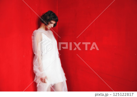 Woman in white dress posing against bright red wall in artistic fashion display 125122817