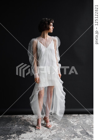 Elegant model showcases sheer designer dress against a minimalist backdrop in a fashion studio Elegant model showcases sheer designer dress against a minimalist backdrop in a fashion studio 125122821
