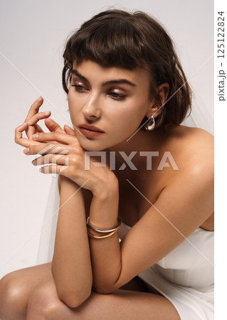Elegant model poses with minimal accessories in a soft studio setting during a fashion photoshoot Elegant model poses with minimal accessories in a soft studio setting during a fashion photoshoot 125122824