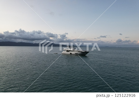 Luxury yacht sailing on calm waters near distant mountains at sunset Luxury yacht sailing on calm waters near distant mountains at sunset 125122916