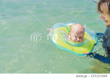 Father and newborn son swimming in the turquoise sea. Baby floating in an inflatable neck ring. Family bonding, fatherhood, and baby first water experience concept 125123364