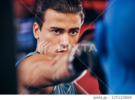 Fitness, boxing and athlete training at a gym for a fighting match with a punching bag and gloves. Motivation, martial arts and man boxer or fighter practicing for MMA competition at a sports center. Fitness, boxing and athlete training at a gym for a fighting match with a punching bag and gloves. Motivation, martial arts and man boxer or fighter practicing for MMA competition at a sports center. 125123604