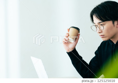 コーヒーを飲みながらパソコンを見る若い男性 コーヒーを飲みながらパソコンを見る若い男性 125125010