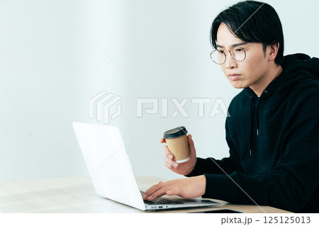 コーヒーを飲みながらパソコンを見る若い男性 コーヒーを飲みながらパソコンを見る若い男性 125125013