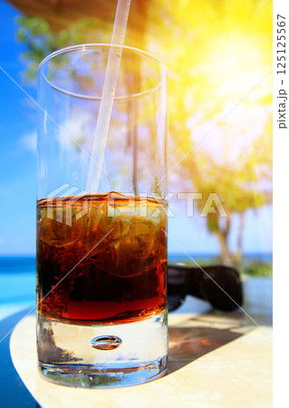 Glass of soda with a straw in it on table. Sunset time with shining sun on the glass 125125567