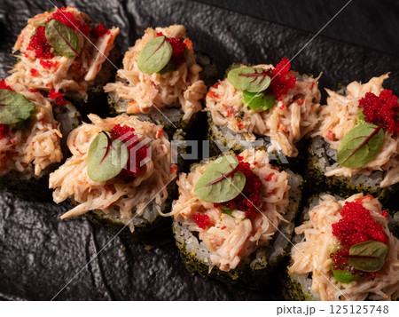 Japanese cuisine. Sushi rolls adorned with roe on a black platter Japanese cuisine. Sushi rolls adorned with roe on a black platter 125125748