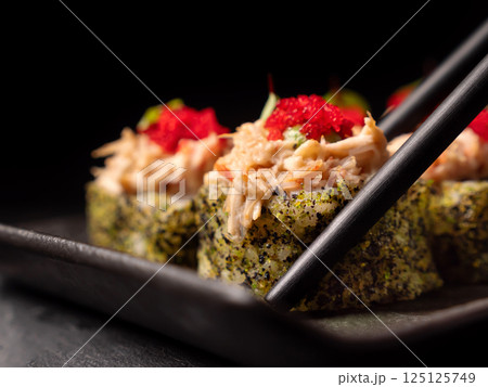 Japanese cuisine. Sushi rolls holding by chopsticks  a black platter, 125125749