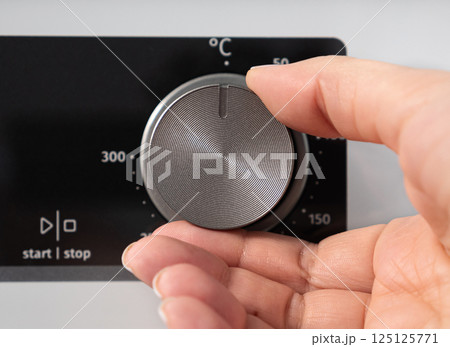 Woman adjusting modern white oven in kitchen. Female hand pushing and turning knobs on oven control panel Woman adjusting modern white oven in kitchen. Female hand pushing and turning knobs on oven control panel 125125771