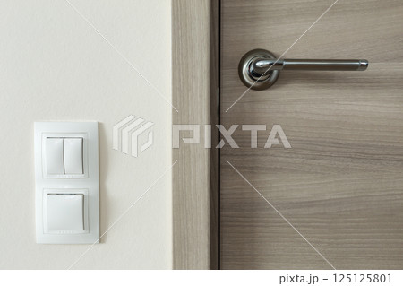 Door handle and white lighting switches on wall 125125801