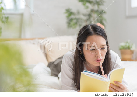 ベッドで寝そべり手帳を見る女性｜日記読書｜健康的な暮らしイメージ｜ウェルビー女子｜ウェルビーイング 125125914