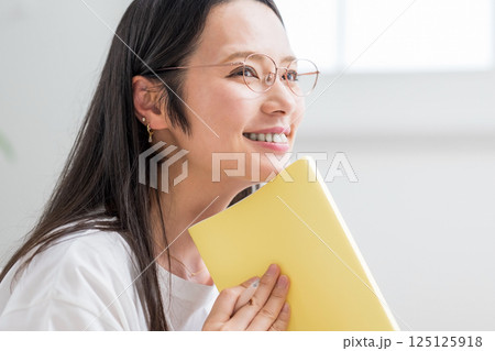 室内で手帳を見る笑顔のメガネ女性｜日記読書｜健康的な暮らしイメージ｜ウェルビー女子｜ウェルビーイング 125125918