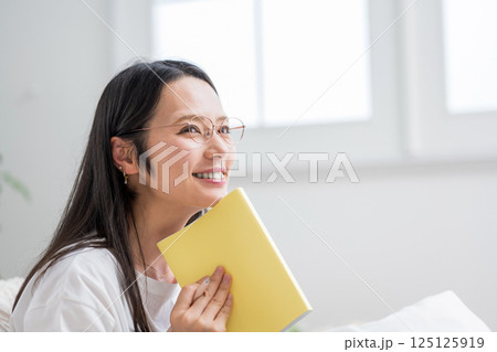 室内で手帳を見る笑顔のメガネ女性｜日記読書｜健康的な暮らしイメージ｜ウェルビー女子｜ウェルビーイング 125125919
