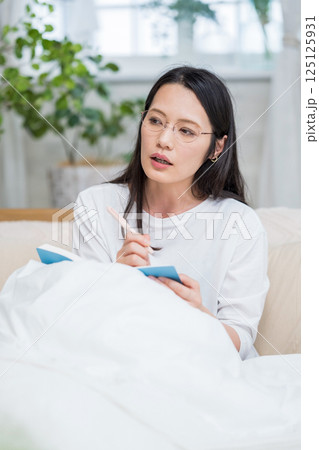 ベッドで手帳を見て考えるメガネ女性|日記|健康的な暮らしイメージ|ウェルビー女子|ウェルビーイング ベッドで手帳を見て考えるメガネ女性|日記|健康的な暮らしイメージ|ウェルビー女子|ウェルビーイング 125125931