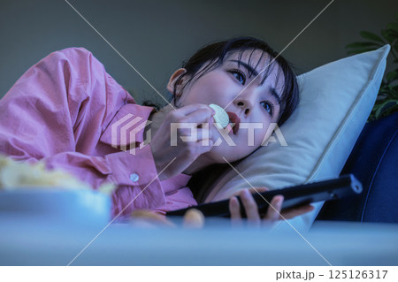 テレビを見ながらお菓子を食べる女性 125126317