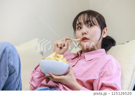 テレビを見ながらお菓子を食べる女性 テレビを見ながらお菓子を食べる女性 125126520