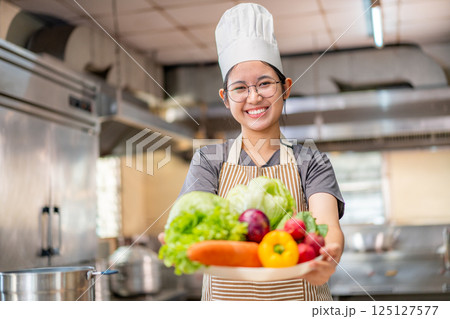 Smiling Young Chef Presenting Fresh Vegetables in Kitchen Smiling Young Chef Presenting Fresh Vegetables in Kitchen 125127577
