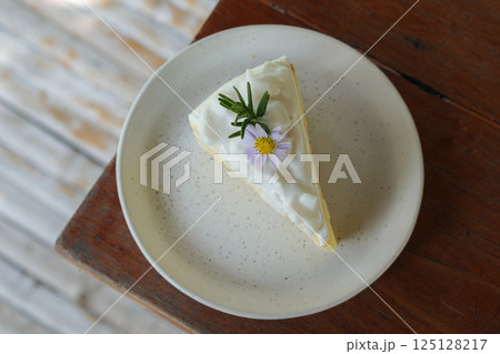 top view Coconut cake decorated with flowers and green leaves on a ceramic plate on a wooden table, blur bamboo floor background, food, dessert, copy space top view Coconut cake decorated with flowers and green leaves on a ceramic plate on a wooden table, blur bamboo floor background, food, dessert, copy space 125128217