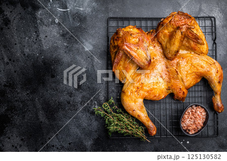 Roasted Spatchcock chicken with herbs and spices, poultry meat on steel rack. black background. top view Roasted Spatchcock chicken with herbs and spices, poultry meat on steel rack. black background. top view 125130582