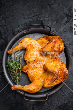 Roasted chicken Tabaka with herbs and spices, poultry meat on steel tray. black background. top view Roasted chicken Tabaka with herbs and spices, poultry meat on steel tray. black background. top view 125130598