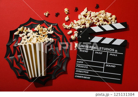 Clapperboard, paper cup with popcorn and Halloween decorations on red background, top view Clapperboard, paper cup with popcorn and Halloween decorations on red background, top view 125131384