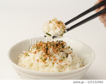 鮭と海苔のふりかけをかけた温かいご飯を箸で持ち上げる 125132082
