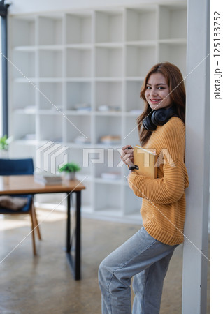 happy young woman with headphones is immersed in a book, happily learning 125133752