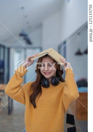 happy young woman with headphones is immersed in a book, happily learning 125133756