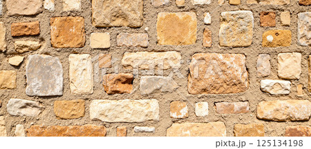 Close-up view of rough orange and yellow bricks with cement joints, aged vintage wall texture, natural stone structure background for design, restoration, construction 125134198
