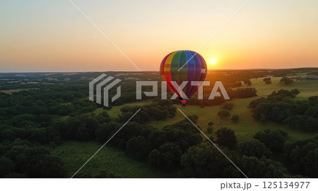 Colorful hot air balloon soaring over scenic landscape at sunset. 125134977