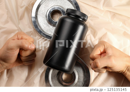 Black plastic jar, sport equipment and male hands on beige background, top view Black plastic jar, sport equipment and male hands on beige background, top view 125135145