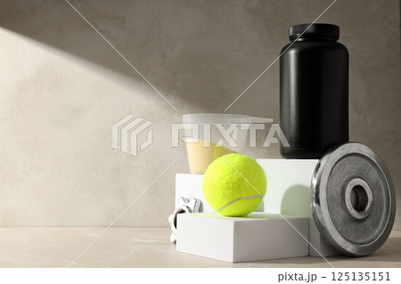 Black plastic jar, measuring cup with powder and sport equipment on beige background, space for text 125135151