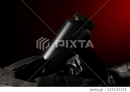Black plastic jar in charcoal on black background, close up 125135152