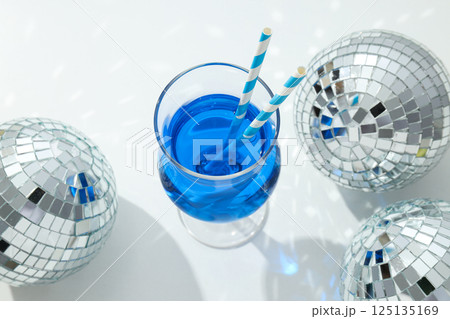 Blue cocktail with straws in glass and disco balls on white background, top view Blue cocktail with straws in glass and disco balls on white background, top view 125135169