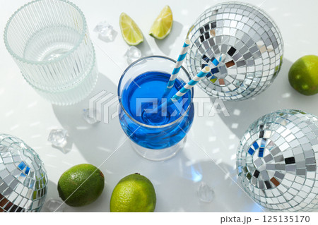 Blue cocktail in glass, limes, ice cubes and disco balls on white background, top view 125135170