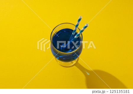 Blue cocktail with straws in glass on yellow background, top view 125135181