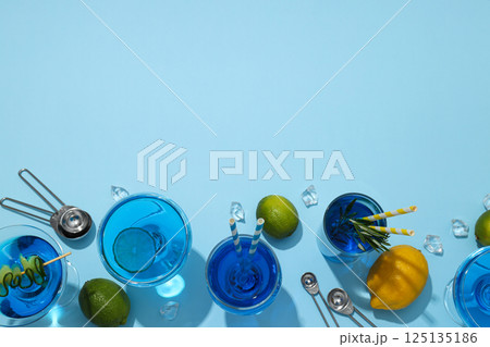 Blue drink in cocktail glasses, lemons, limes and ice cubes on blue background, space for text Blue drink in cocktail glasses, lemons, limes and ice cubes on blue background, space for text 125135186