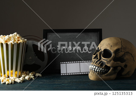 Blackboard, skull, reel and paper cup with popcorn on dark background 125135313