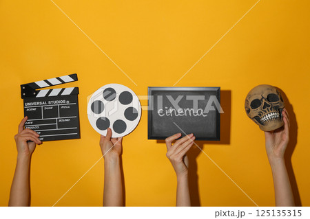 Blackboard with text, reel, skull and clapperboard in hands on yellow background Blackboard with text, reel, skull and clapperboard in hands on yellow background 125135315