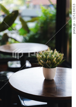 A potted plant sits on a wooden table in a restaurant. The plant is green and he is a fake 125138313