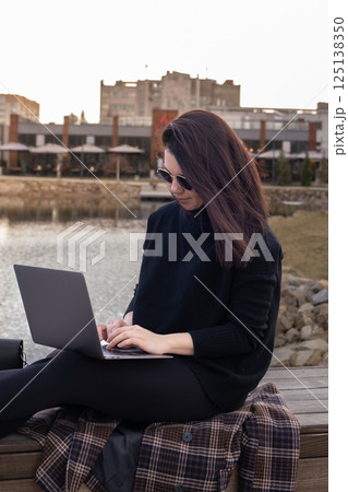 Woman Using Laptop by Pond in Urban Setting 125138350