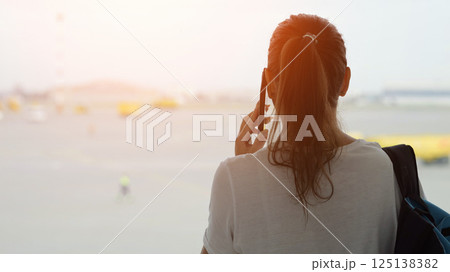 Lady calls on phone looking out window at aircraft movement area Lady calls on phone looking out window at aircraft movement area 125138382