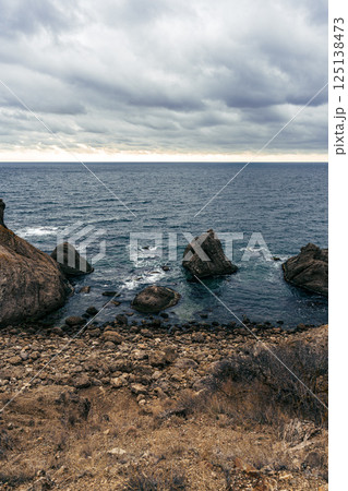 Rocky coastline under a cloudy sky with ocean waves crashing against the shore at dusk Rocky coastline under a cloudy sky with ocean waves crashing against the shore at dusk 125138473