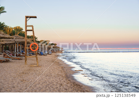 Lifeguard station on a tranquil beach at sunset in a coastal region with gentle waves and lounge chairs Lifeguard station on a tranquil beach at sunset in a coastal region with gentle waves and lounge chairs 125138549