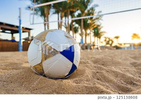 Beach soccer ball resting on sand during sunset with palm trees in the background 125138608
