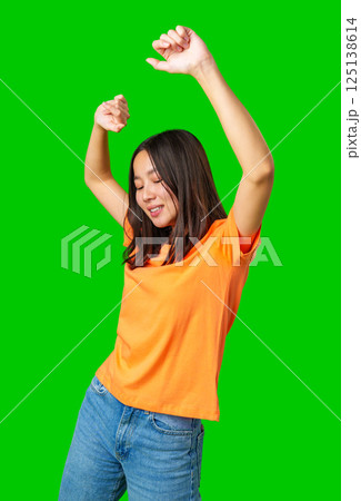 Young woman dancing joyfully in a bright orange shirt against a vibrant green background during a lively moment Young woman dancing joyfully in a bright orange shirt against a vibrant green background during a lively moment 125138614