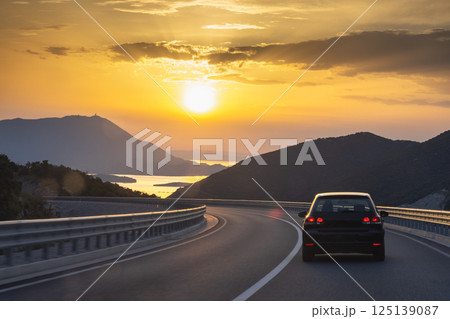 Road on Peljesac peninsula in Croatia, Europe. Scenic Road Trip: Driving into the sunset with mountains and water views on a winding coastal highway. Freedom and adventure awaits! 125139087