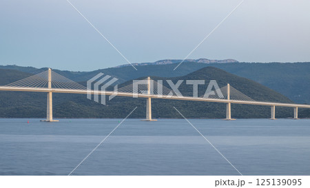 The Peljesac Bridge to Peljesac peninsula in Croatia, Europe. Long cable-stayed bridge spans a serene body of water, seamlessly connecting distant shores against a backdrop of verdant hills. 125139095